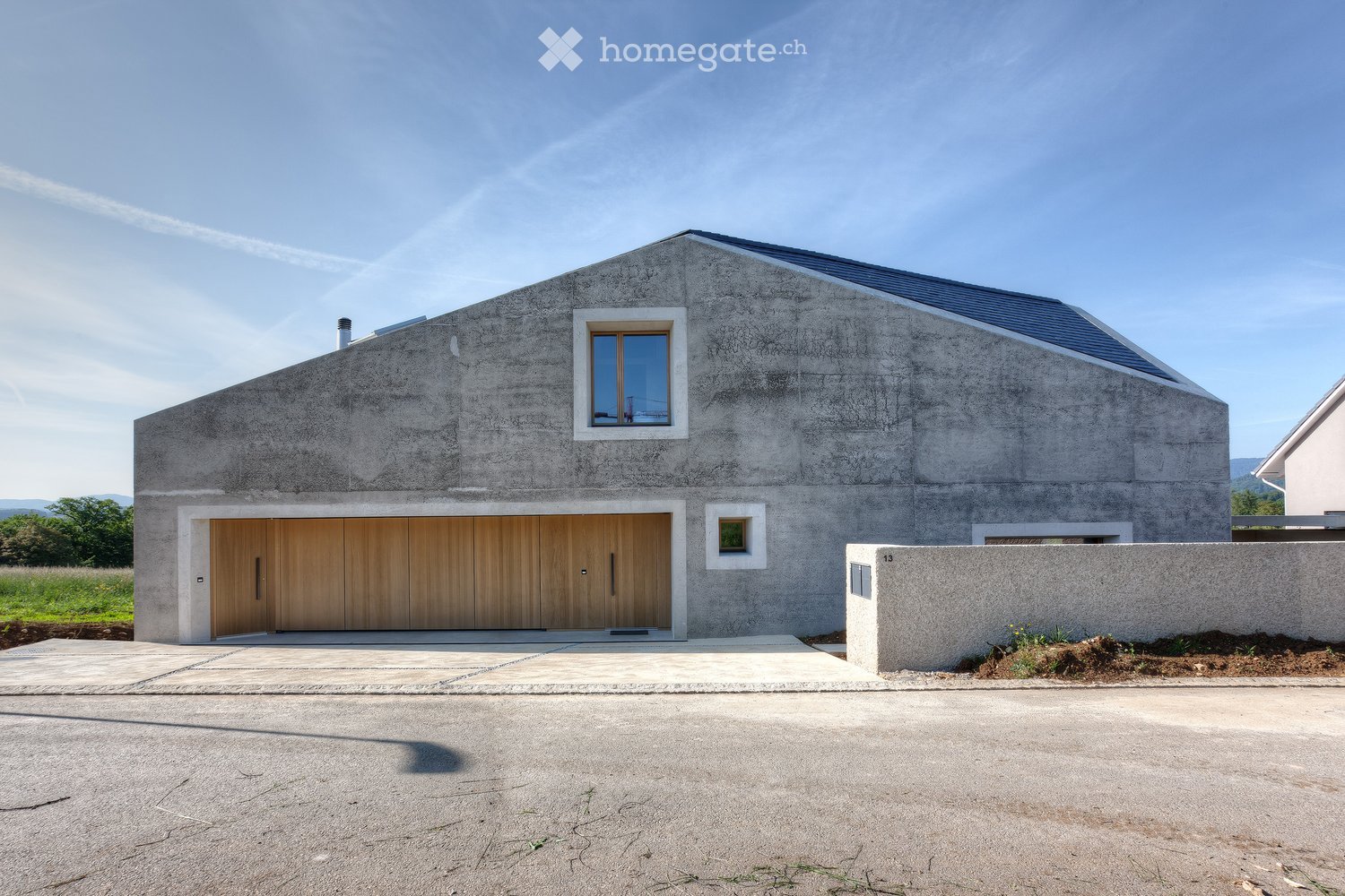 Two-story house with gray concrete exterior, blue roof, wooden garage doors, windows, driveway