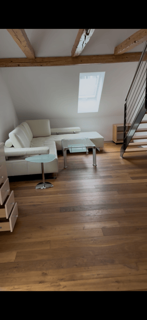 white sofa, glass coffee table, round table, hardwood floor, wooden beams, attic window, wooden staircase