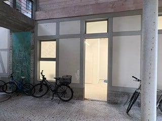 A room with concrete floor, three bicycles parked, open door, windows, and a pillar