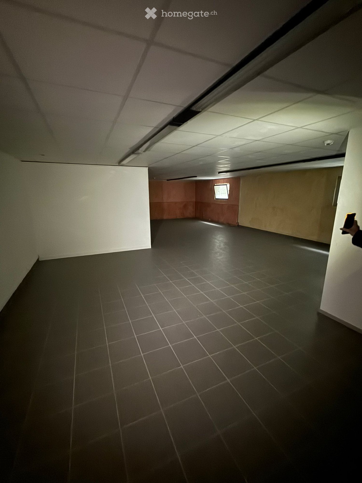Empty room with tiled floor, square lights on ceiling, wall on the left and back
