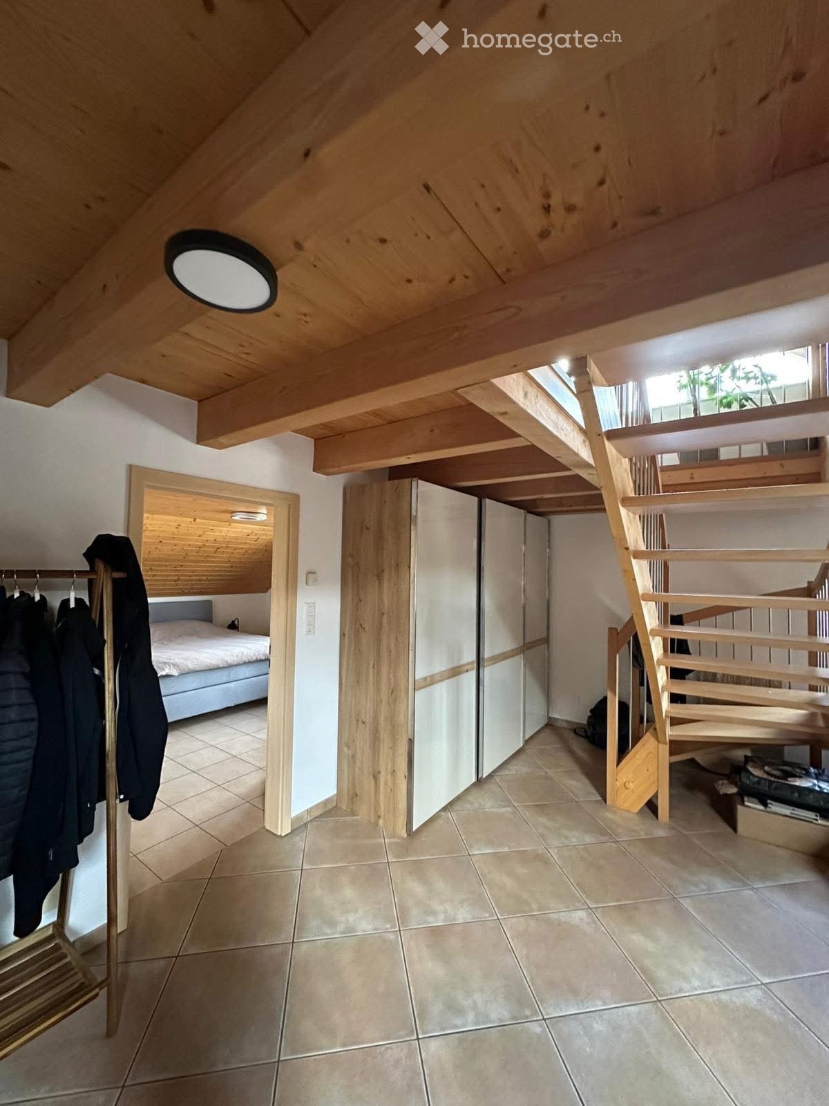 bedroom with a bed, wardrobe, wooden stairs, clothes rack, and ceiling lamp
