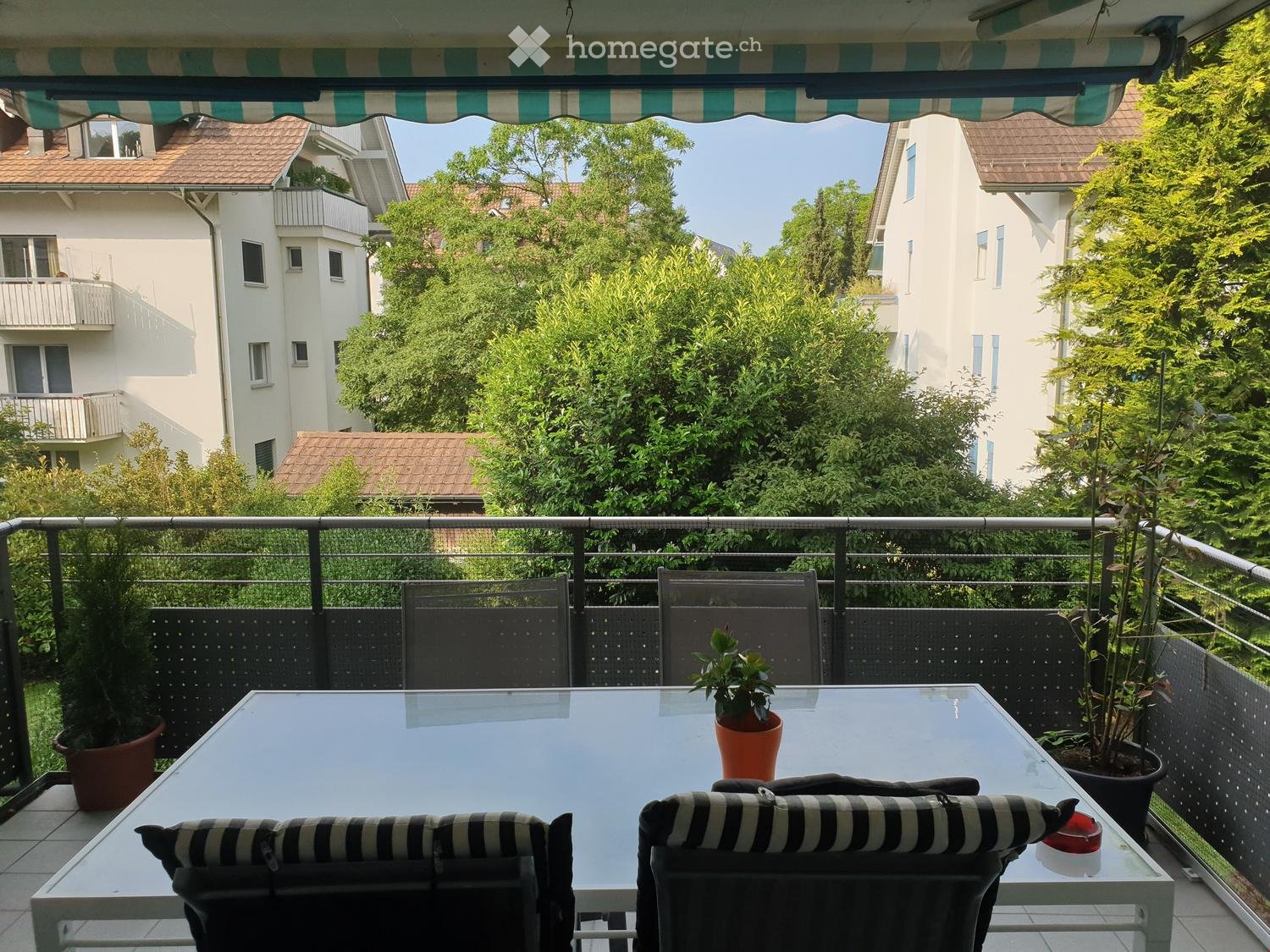 Outdoor table with 4 chairs, balcony, black and white cushions, plants, trees, view of buildings