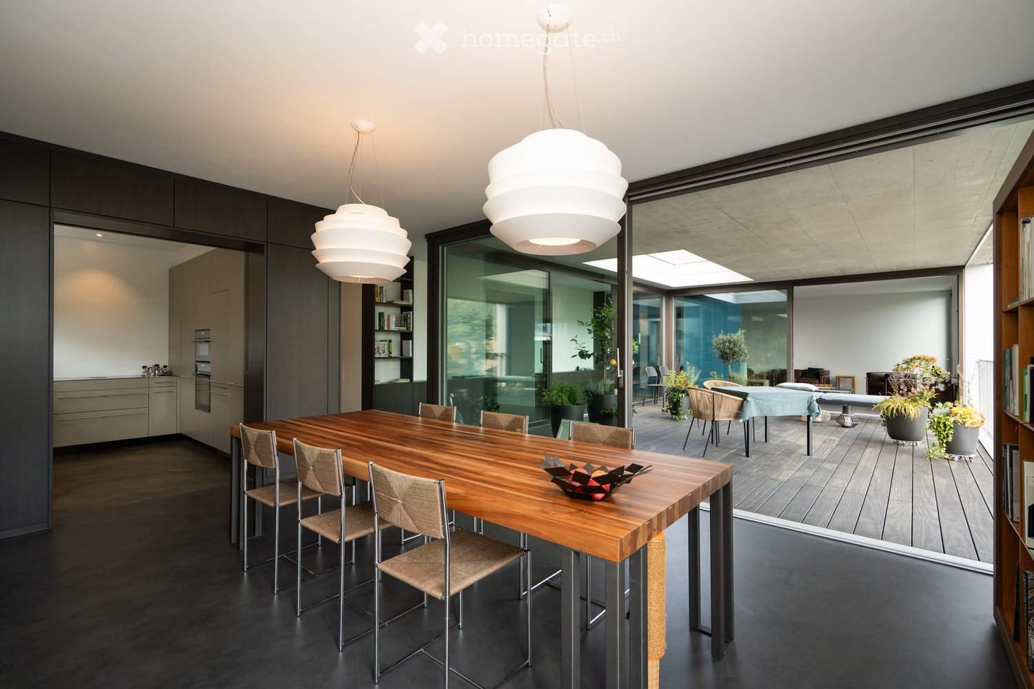 large wooden dining table, modern chairs, large glass doors, balcony, plants, view of the outside