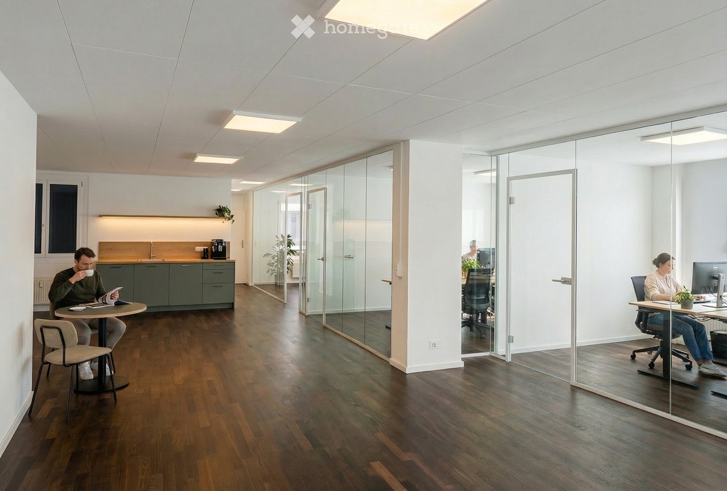 Modern open plan office with glass partitions, wooden floors, central kitchen area, tables with chairs, and employees working at their desks.