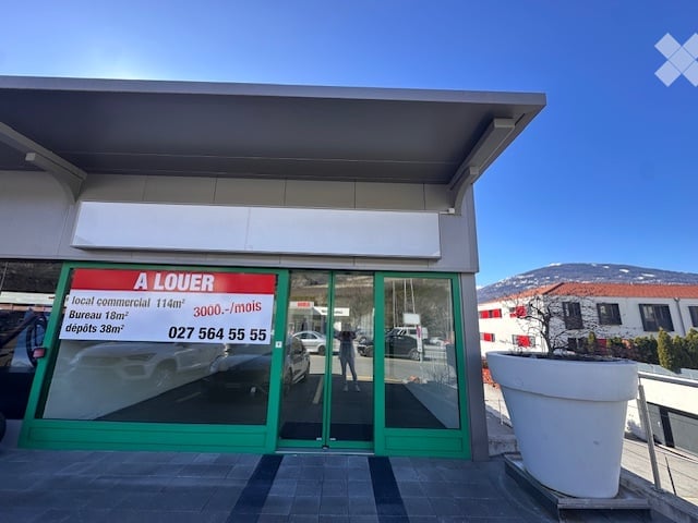 Commercial building with glass doors and windows, green frame, signboard, and a large white planter