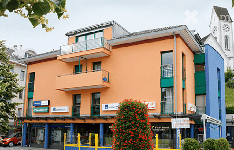 3 story building, orange and blue facade, balconies, shops on the ground floor