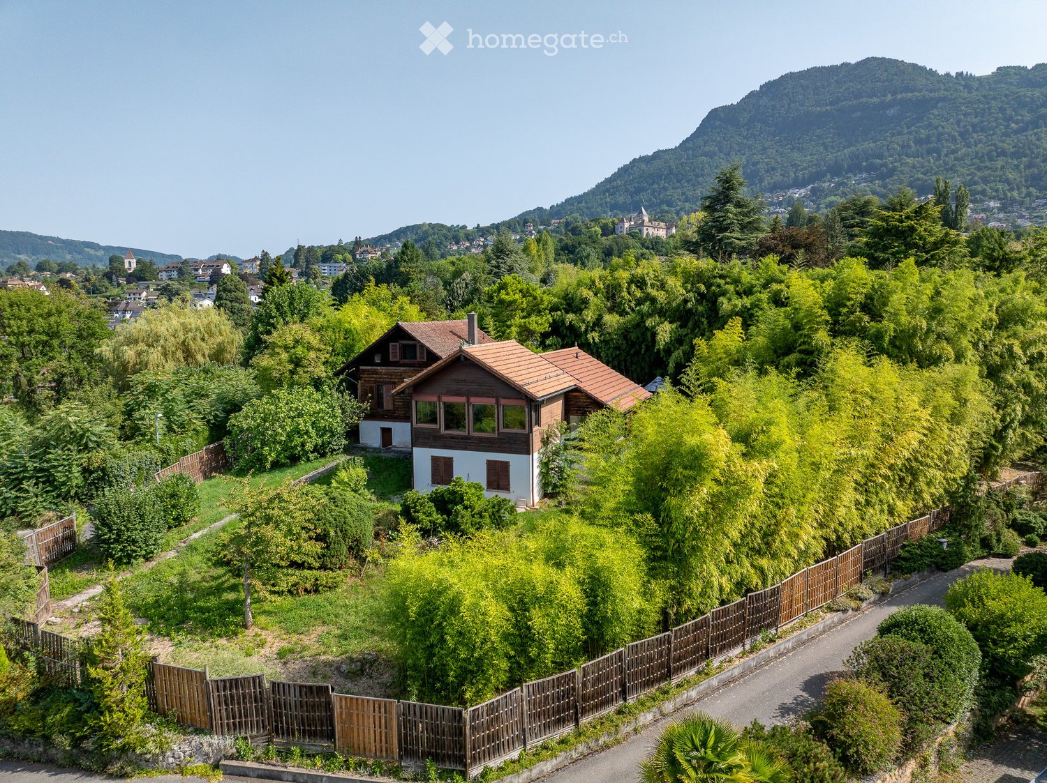 detached house with tiled roof, surrounded by green trees, situated in a scenic area with mountains