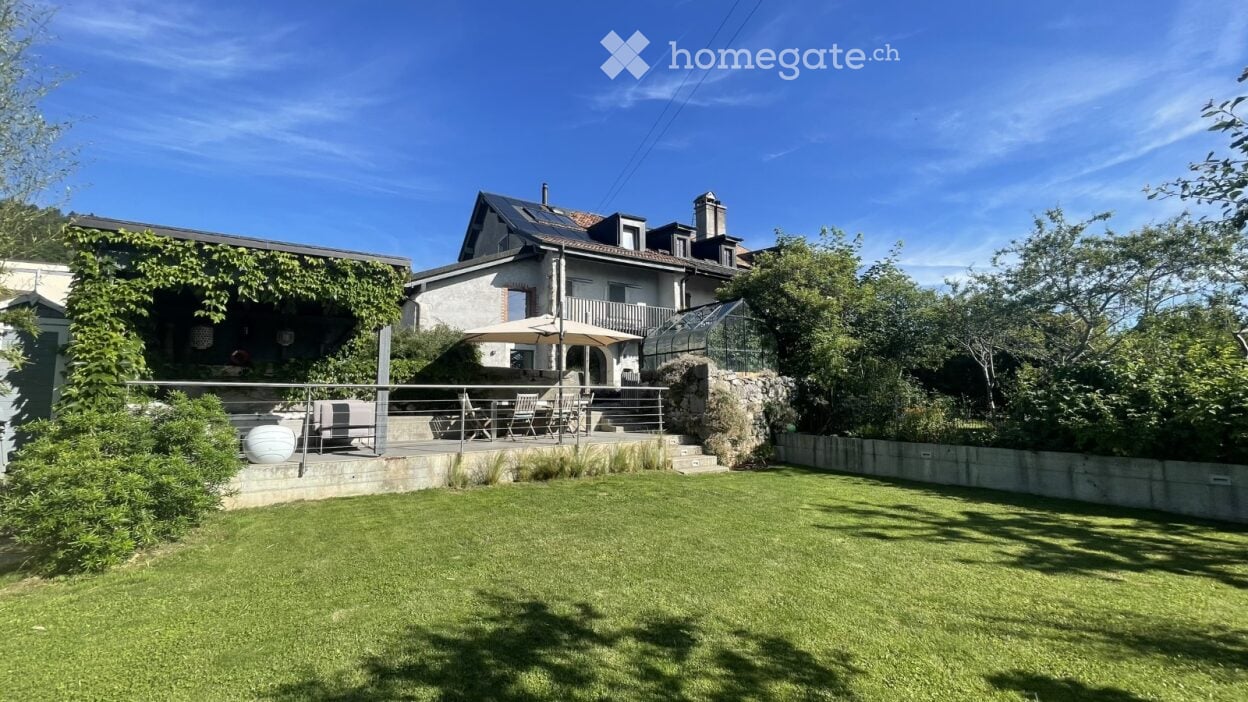 Well-maintained garden with a lawn, patio seating area, and a greenhouse attached to a house.