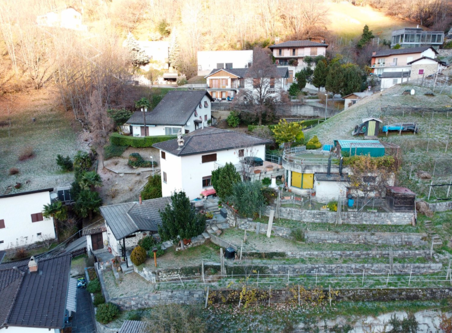 Houses on a hillside, terraced gardens, stone walls, trees, distant mountains