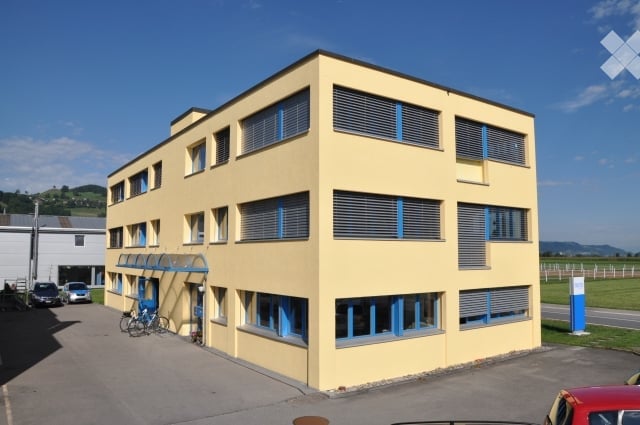 3 story building, yellow exterior, blue windows, parking lot, bicycles