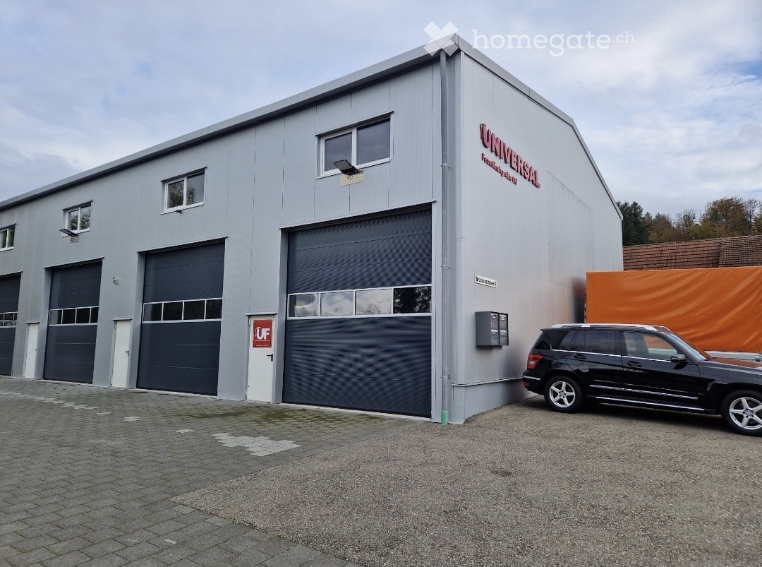 Industrial building with 4 garages, gray exterior, large windows, black SUV parked in front