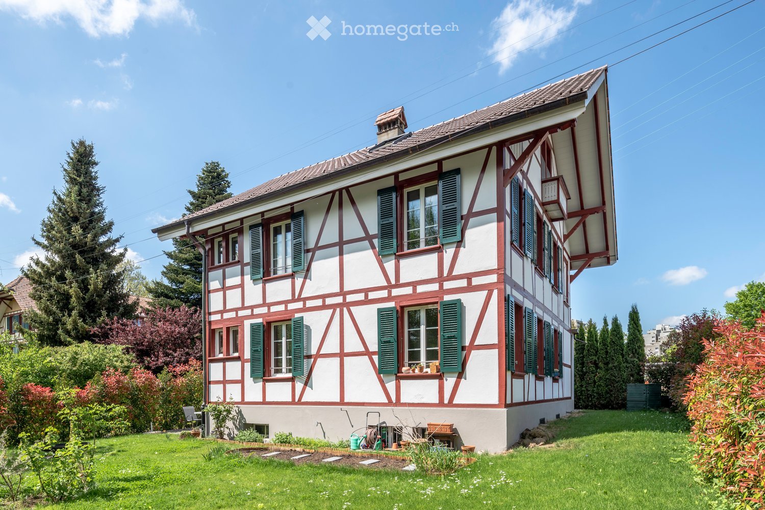 2 story house, white and red exterior, green shutters, raised ground floor, garden, trees