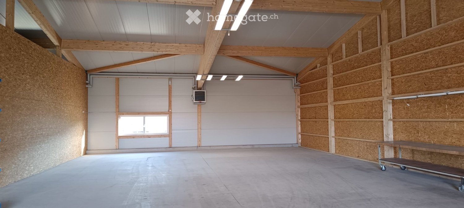 Empty garage with wooden beams, concrete floor, large garage doors, and a small window. No furniture or equipment present.