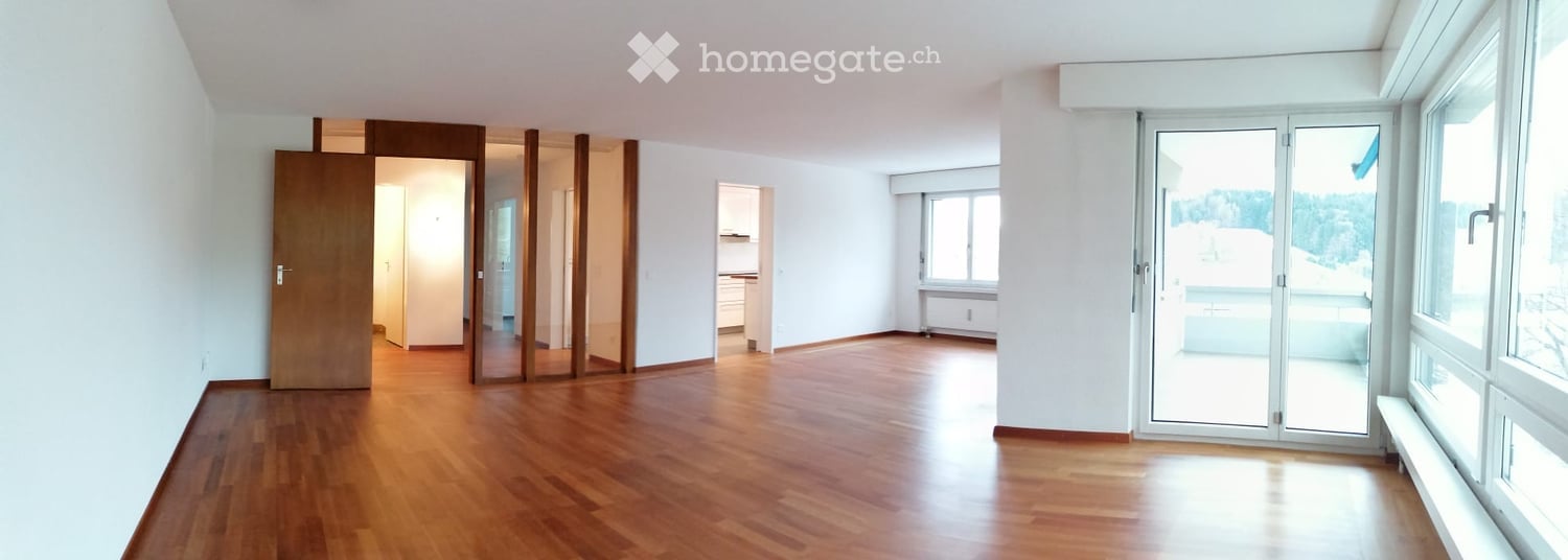 Empty room with wooden flooring, white walls, large windows, and a sliding glass door leading to a balcony.