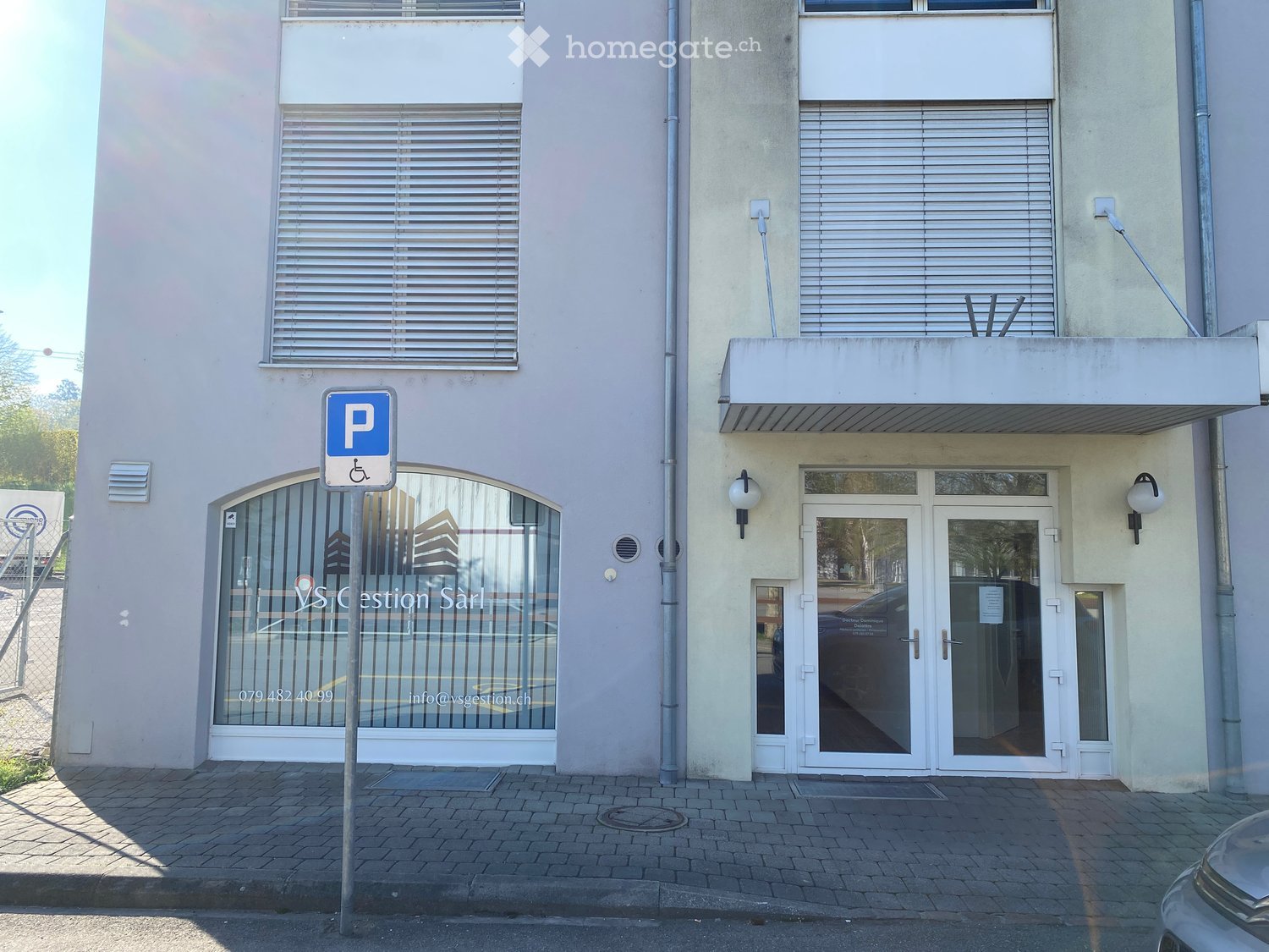 Building. Facade of a building with two entrances, one with a glass door and the other with a glass window. A parking sign is in front of the building.