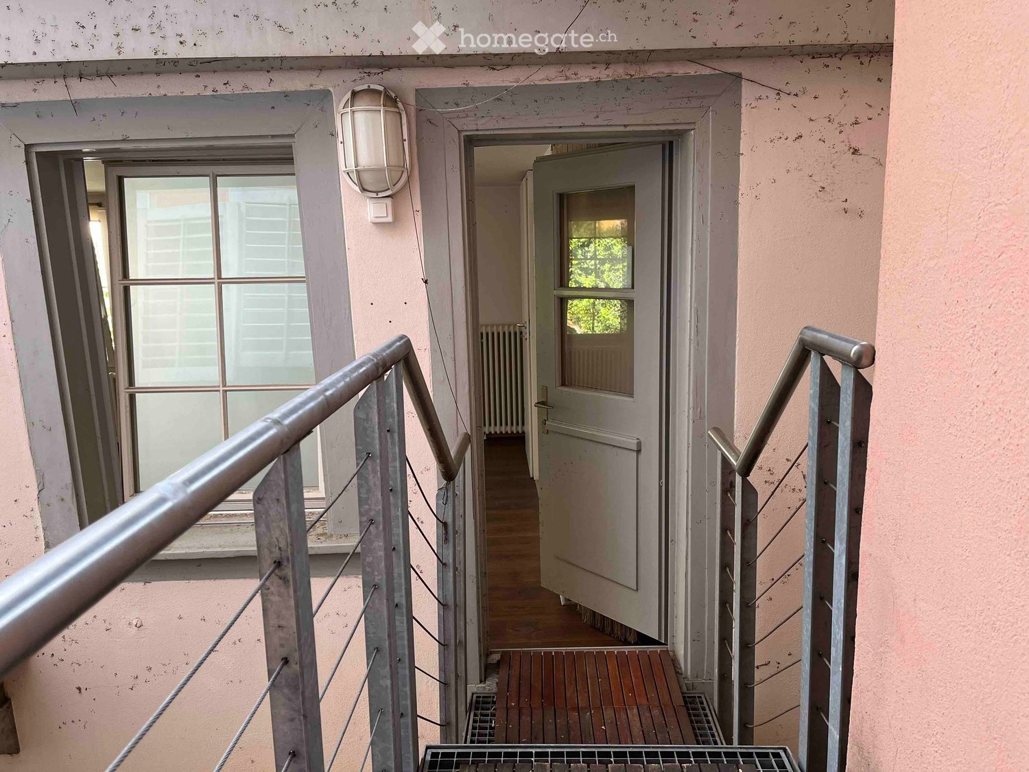 Raised staircase with wooden steps, metal handrails, open door, street lamp, wooden floor