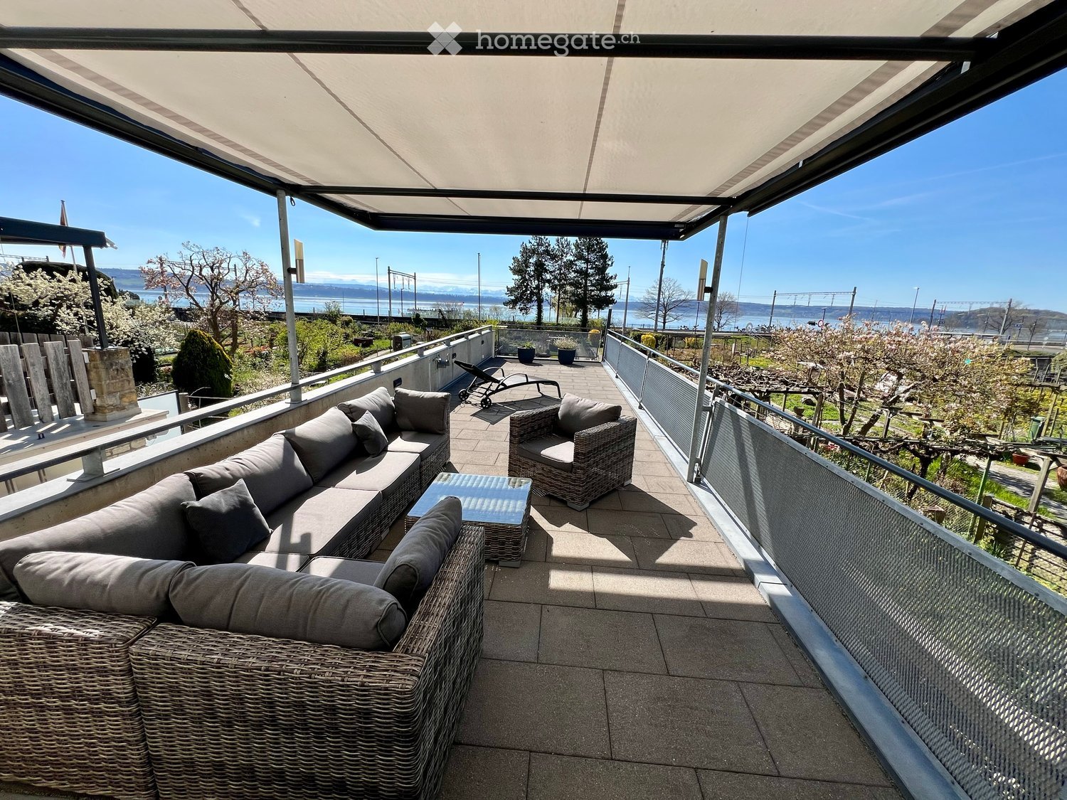 Balcony with a view of the water, featuring a wicker sofa, a wicker chair, and a glass table.