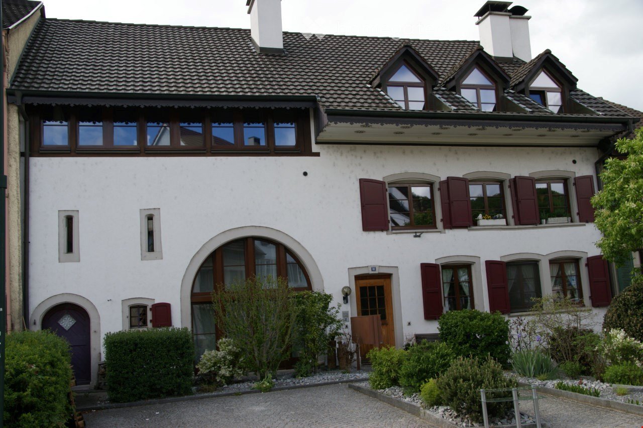 white house, brown roof, arched window, red shutters, purple front door, gravel driveway