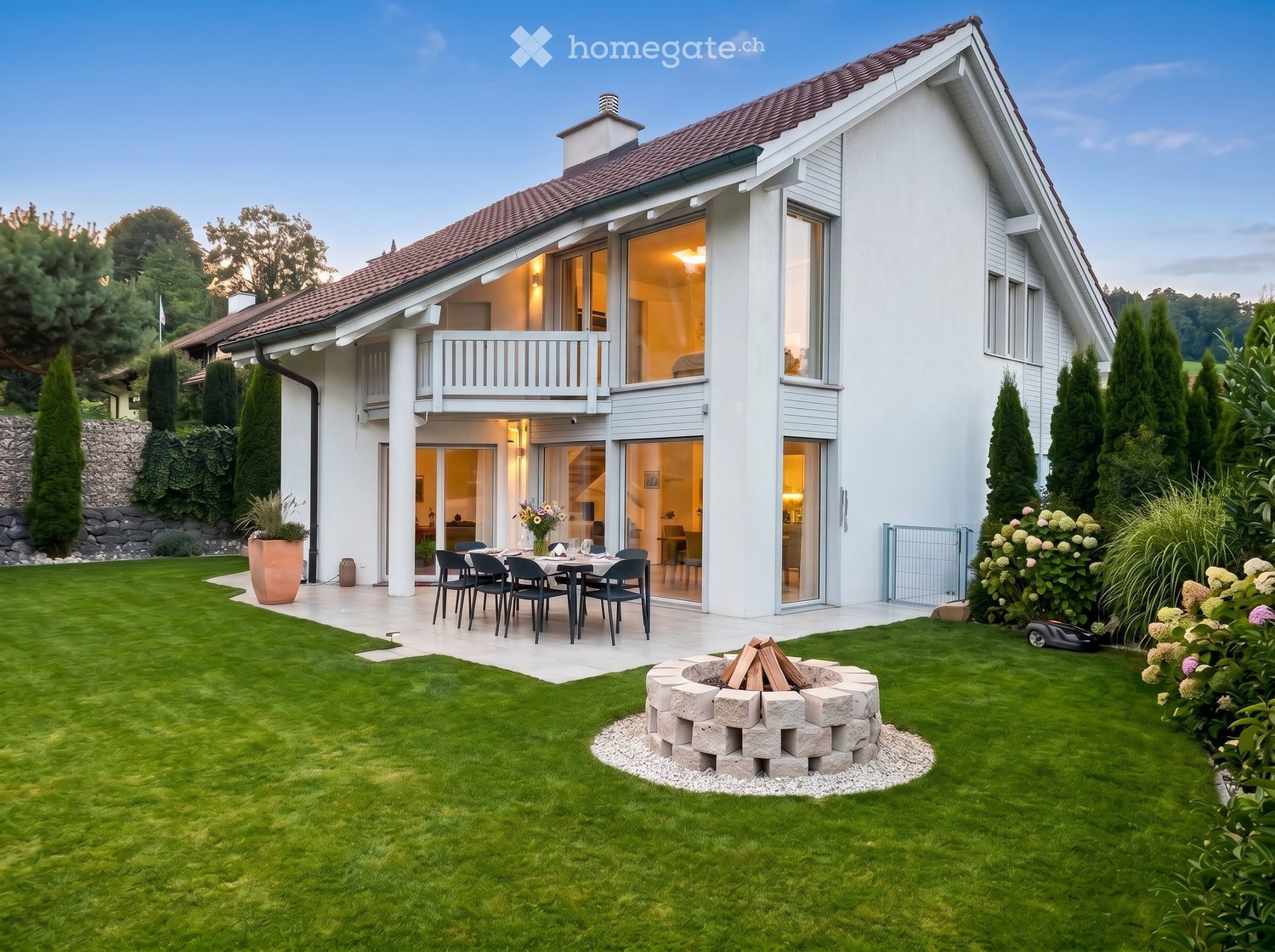 House. Modern two-story house with white exterior, large windows, and a spacious garden featuring a dining set, fire pit, and well-maintained lawn.