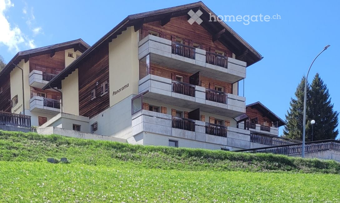 Building. Multi-story wooden building with balconies and a grassy slope in front.