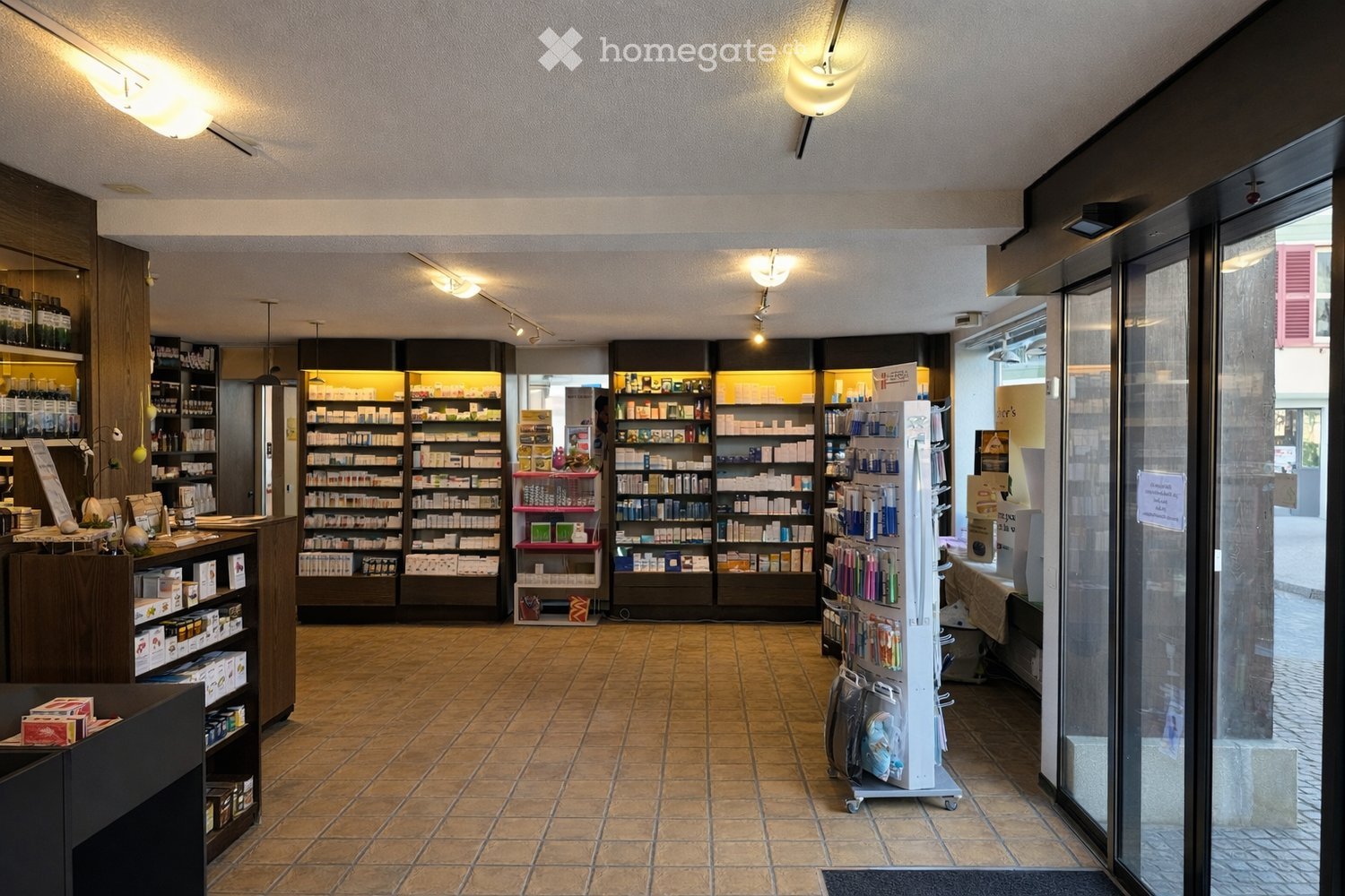 Well-lit interior of a store with tiled floor, shelves stocked with various products, a refrigerator, and a counter area.