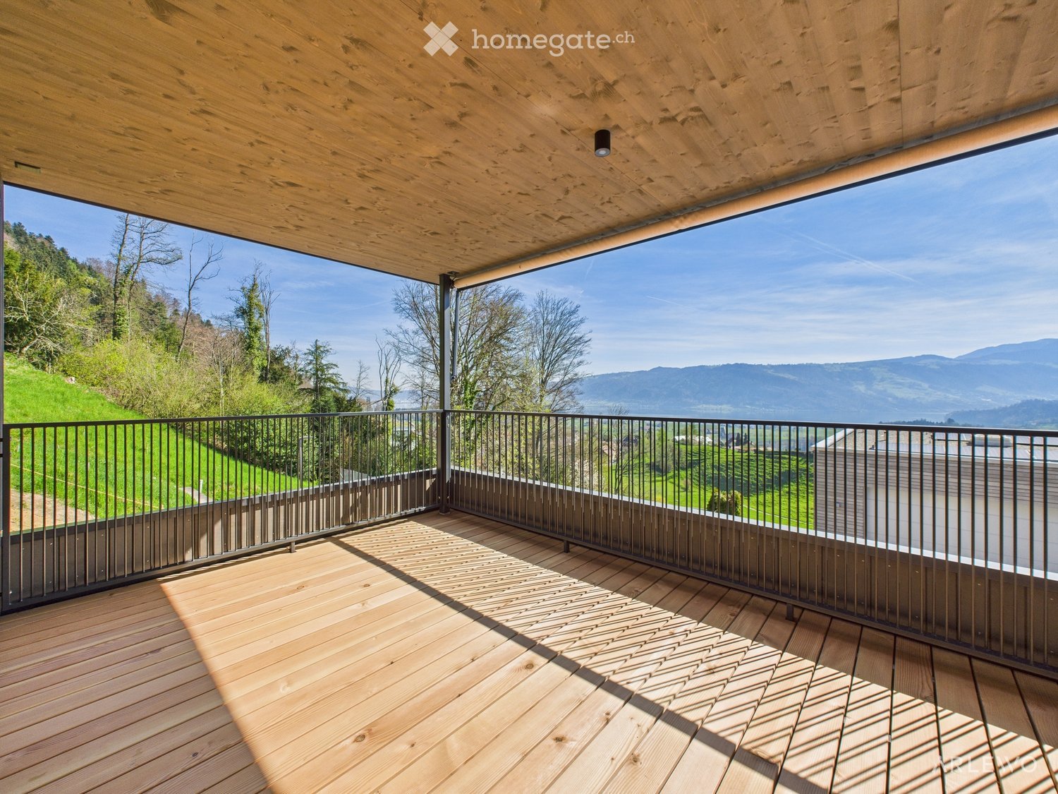 Wooden deck with black metal railing, offering panoramic mountain and valley views.