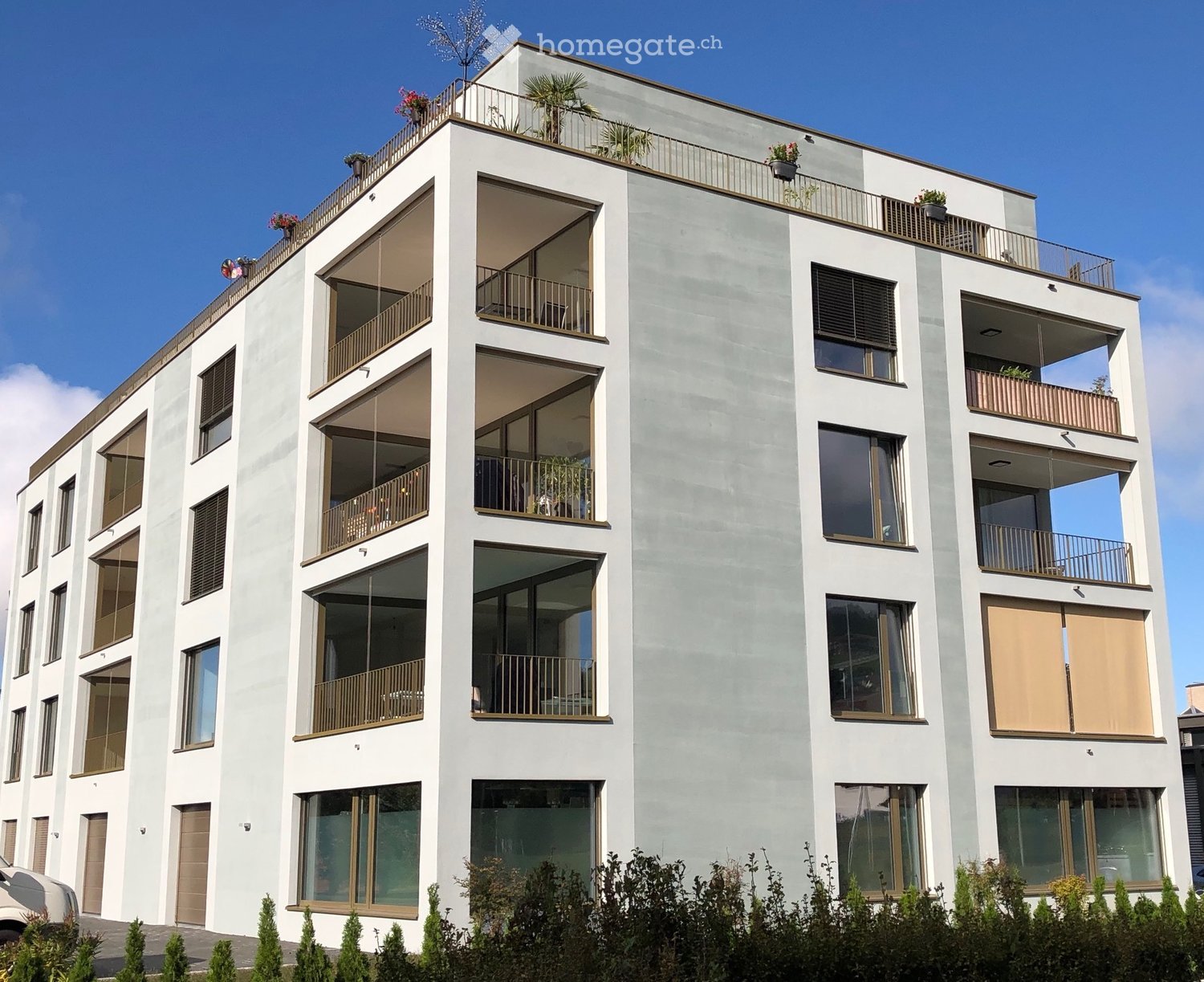 Modern multi-story building with balconies, large windows, and potted plants on balconies.