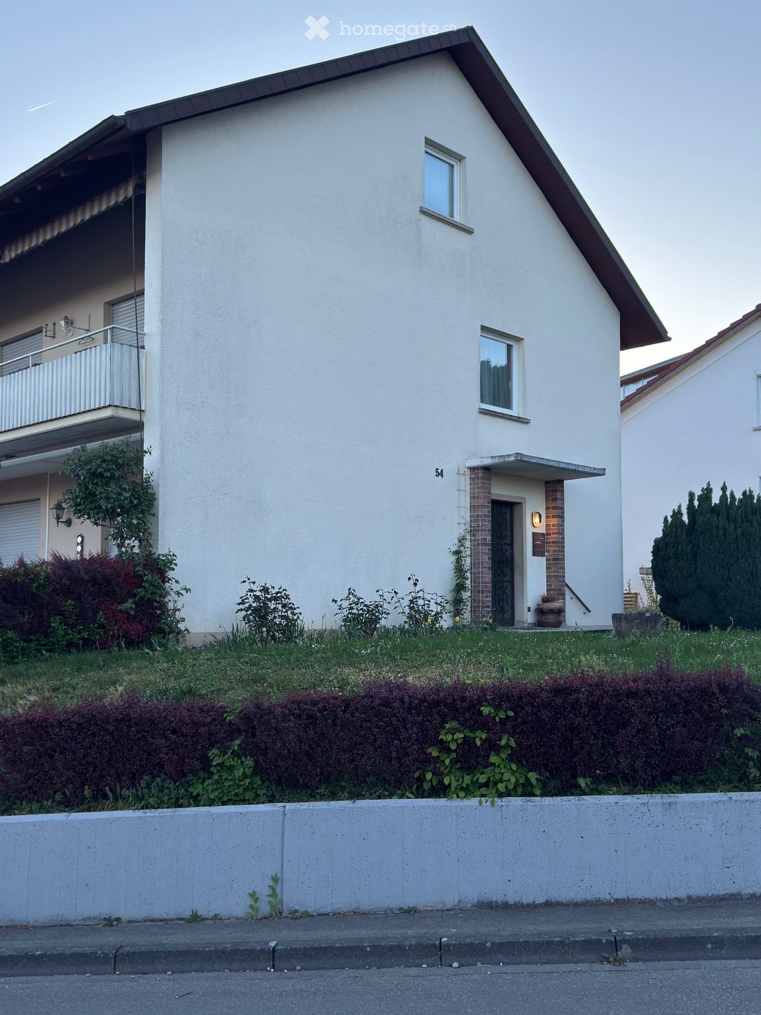 Two-story white house with a pitched roof, balcony, and small garden area.
