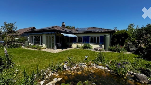 Single-family house with a well-maintained garden, pond, and patio area. The house features a blue shutters and a striped awning over the entrance.