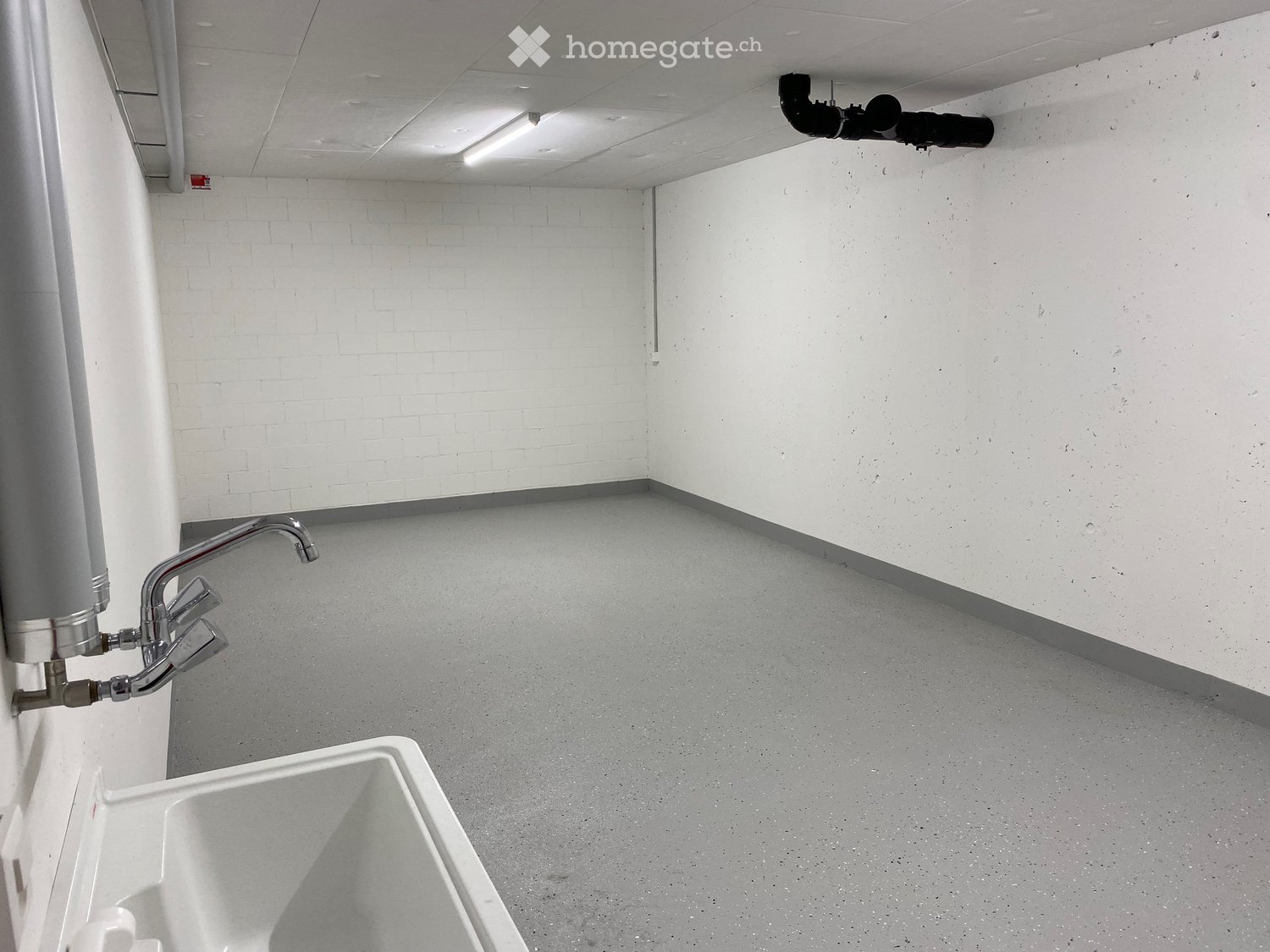Empty room with white brick walls, grey concrete floor, a sink, and a water heater unit on the wall.