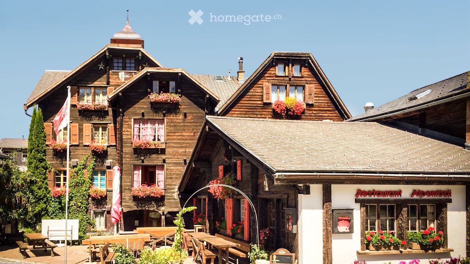 Traditional wooden chalet-style buildings with flower boxes, outdoor seating area, and a restaurant sign reading "Restaurant Alpenrose".