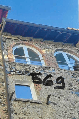 Close-up of a weathered stone building facade with arched windows and the number "569" painted on it.