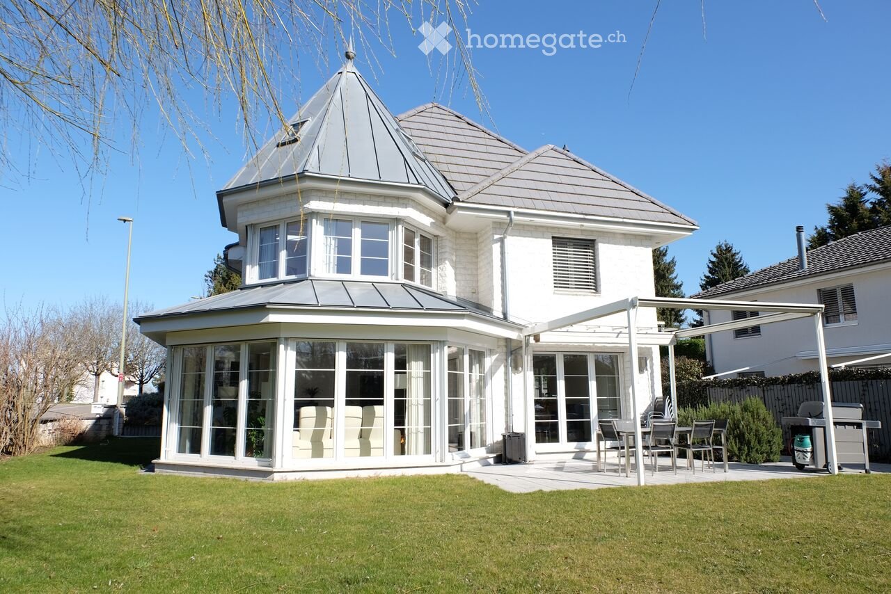 Two-story white house with grey roof, large windows, and a covered patio area with outdoor furniture.