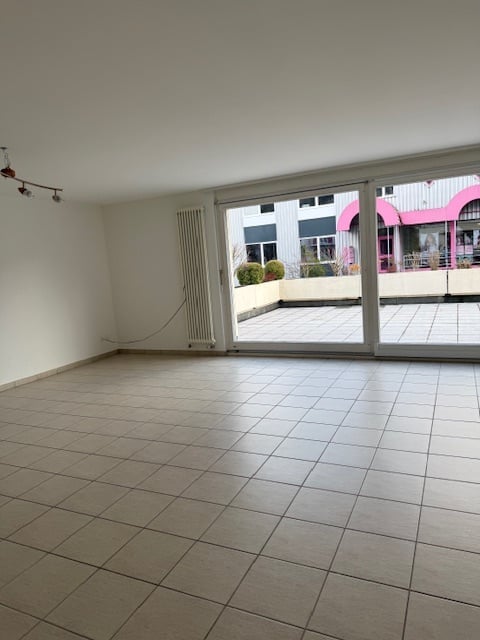 Empty room with tiled floor, large sliding glass doors leading to a balcony or terrace area, white walls, and a radiator visible on one wall.