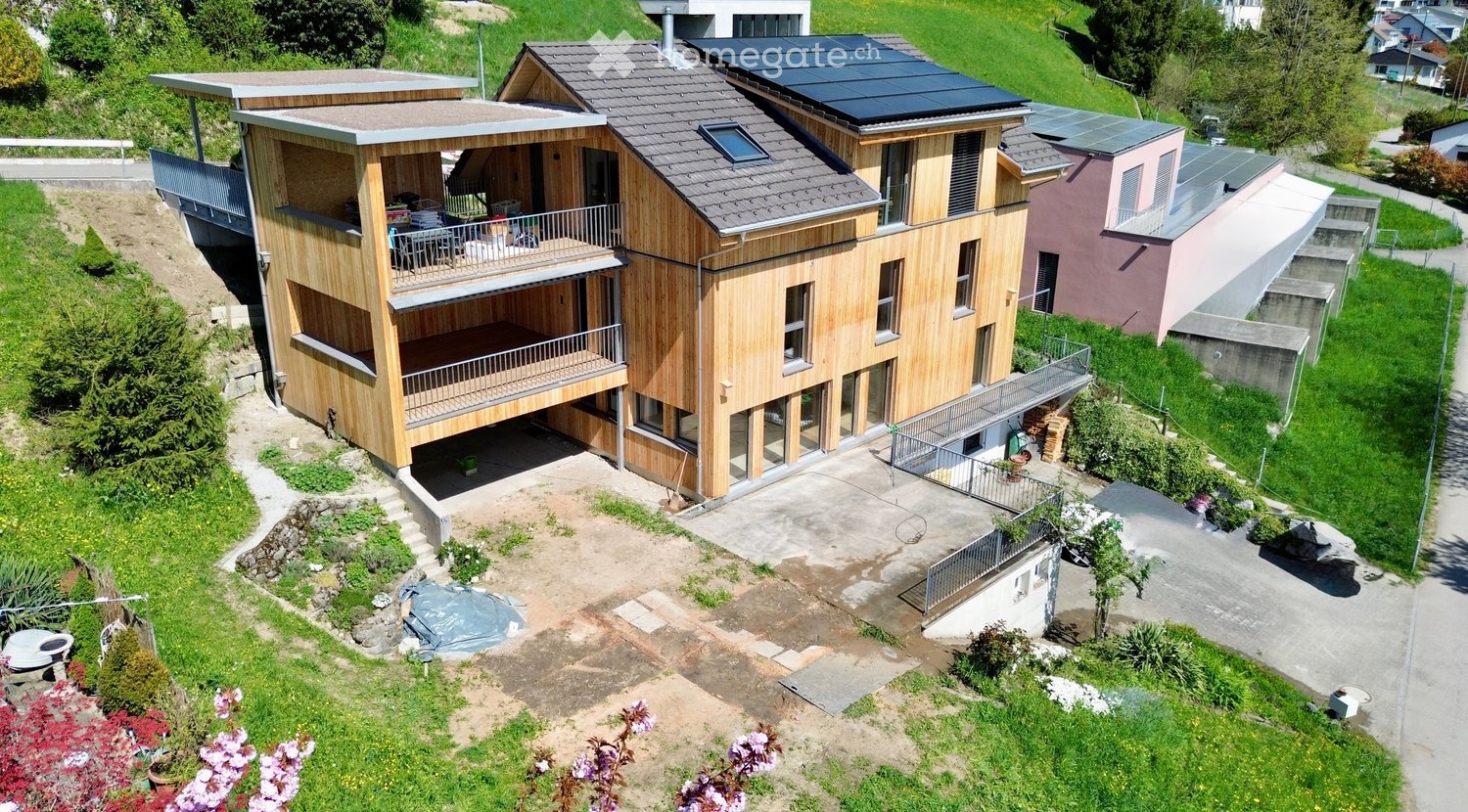 2 story house, wooden exterior, solar panels on the roof, raised ground floor, balcony, driveway, garden