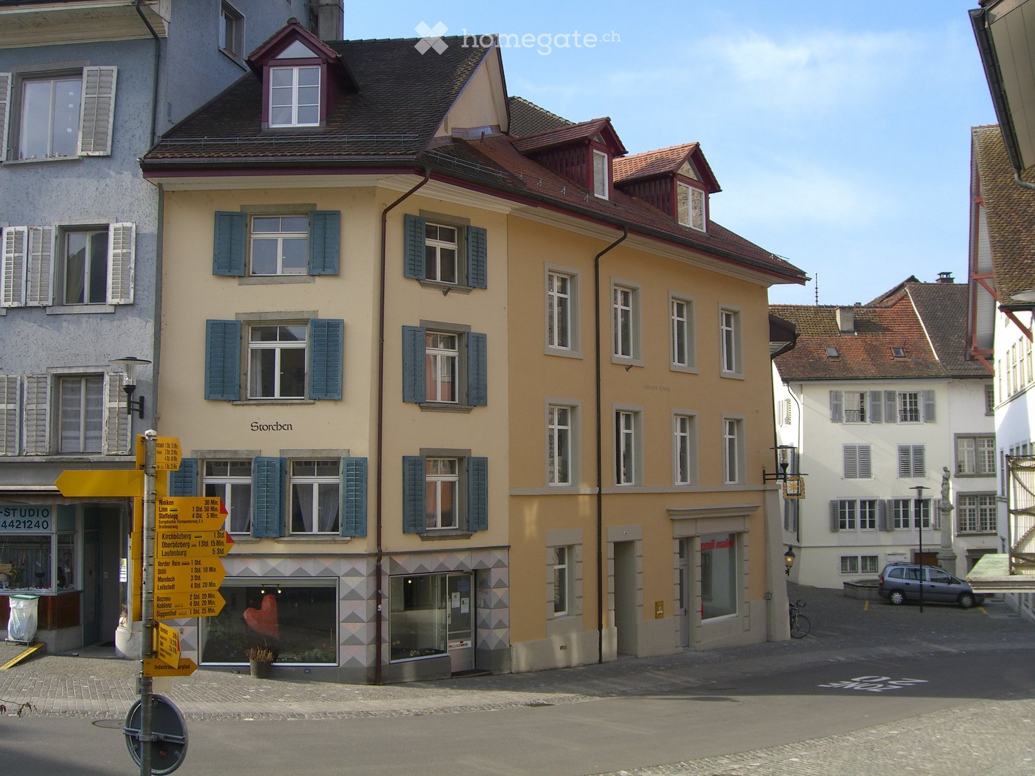 A row of three colorful buildings with traditional European architecture, featuring shutters, signage, and a small storefront with a display window.