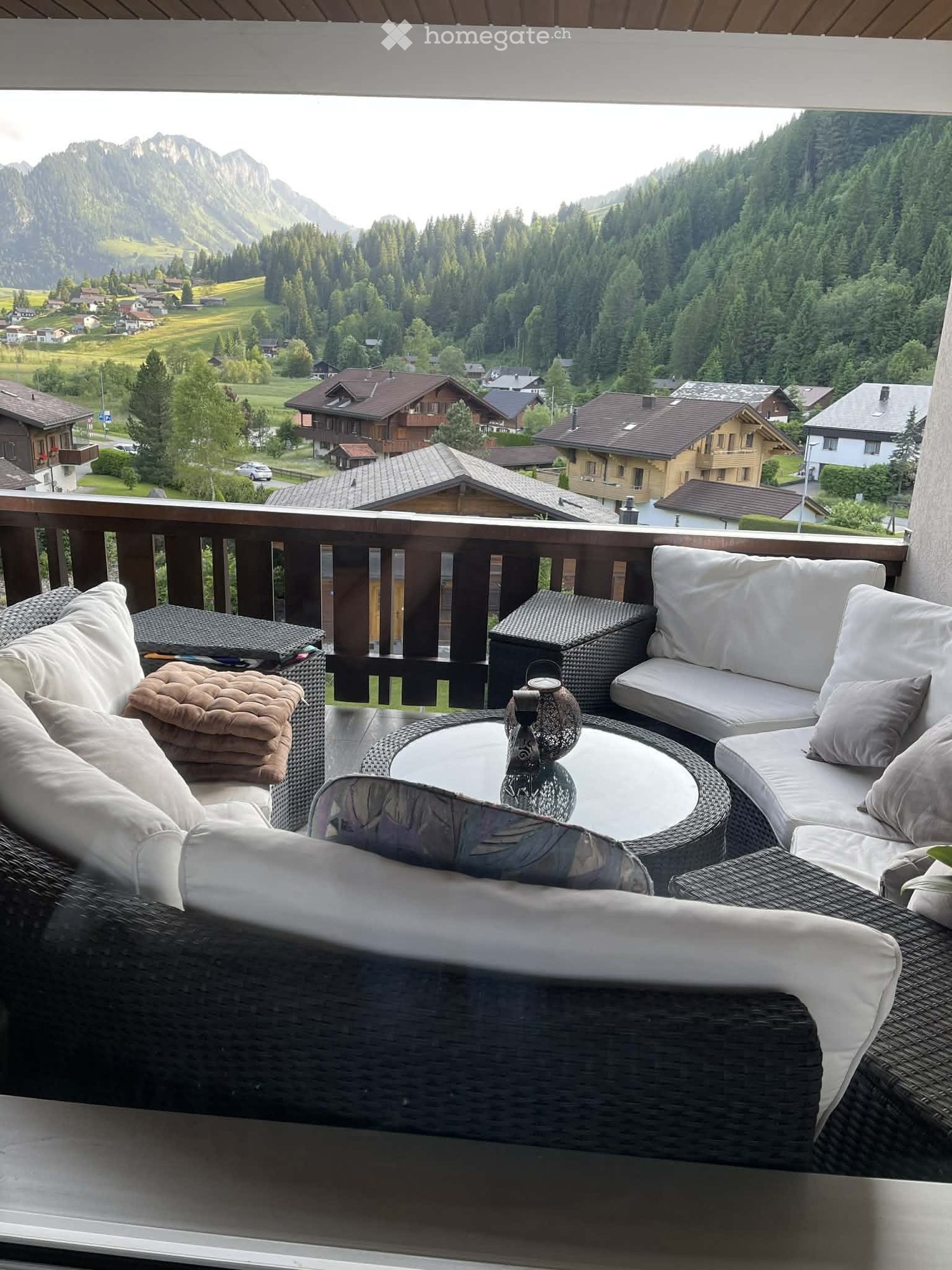 Balcony with wicker furniture, including a sofa, coffee table, and chairs, overlooking a scenic mountain landscape.