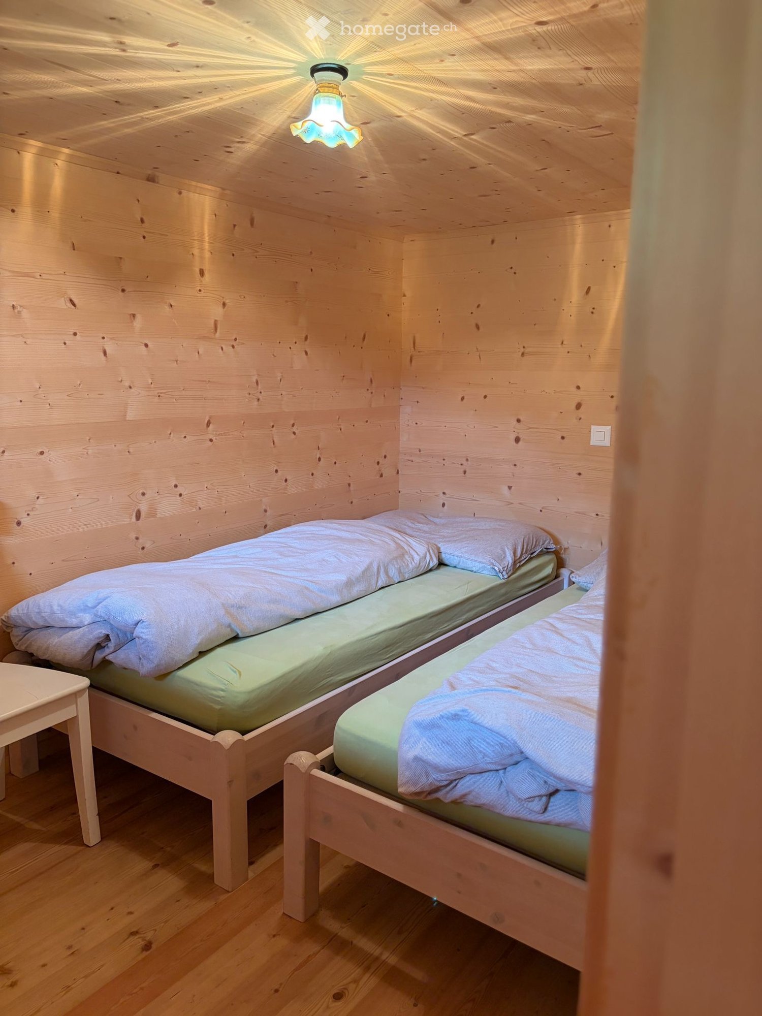 Cozy wooden bedroom with two single beds, light-colored bedding, and a small nightstand.
