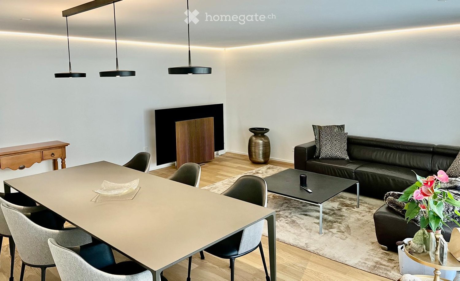 contemporary dining area with a long dining table and chairs, black leather sofa, coffee table, black flat screen TV, decorative items, wooden flooring