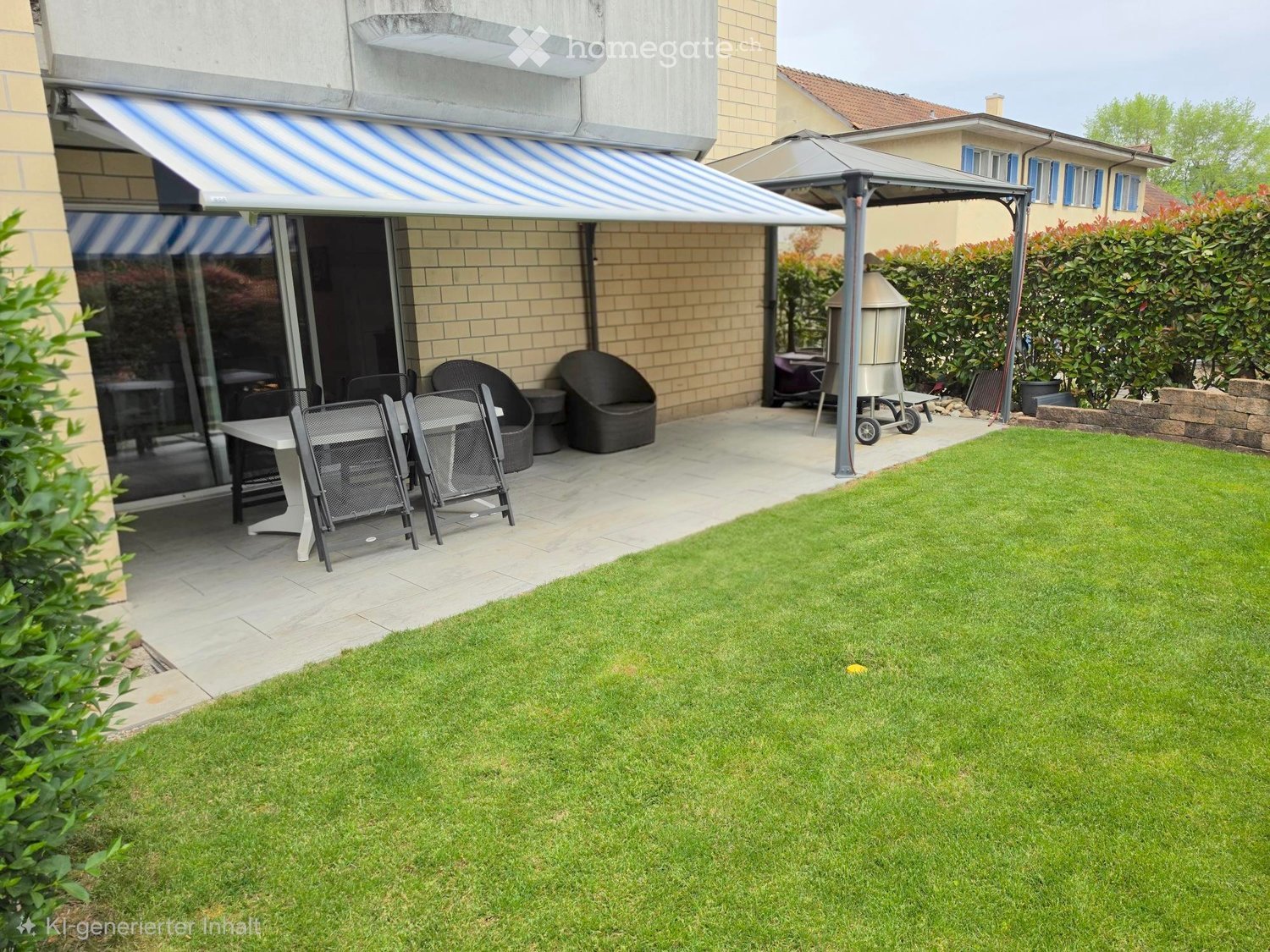 Well-maintained garden with a neatly trimmed lawn, patio area with outdoor furniture including a table, chairs, and an umbrella, and a grill under a covered area.