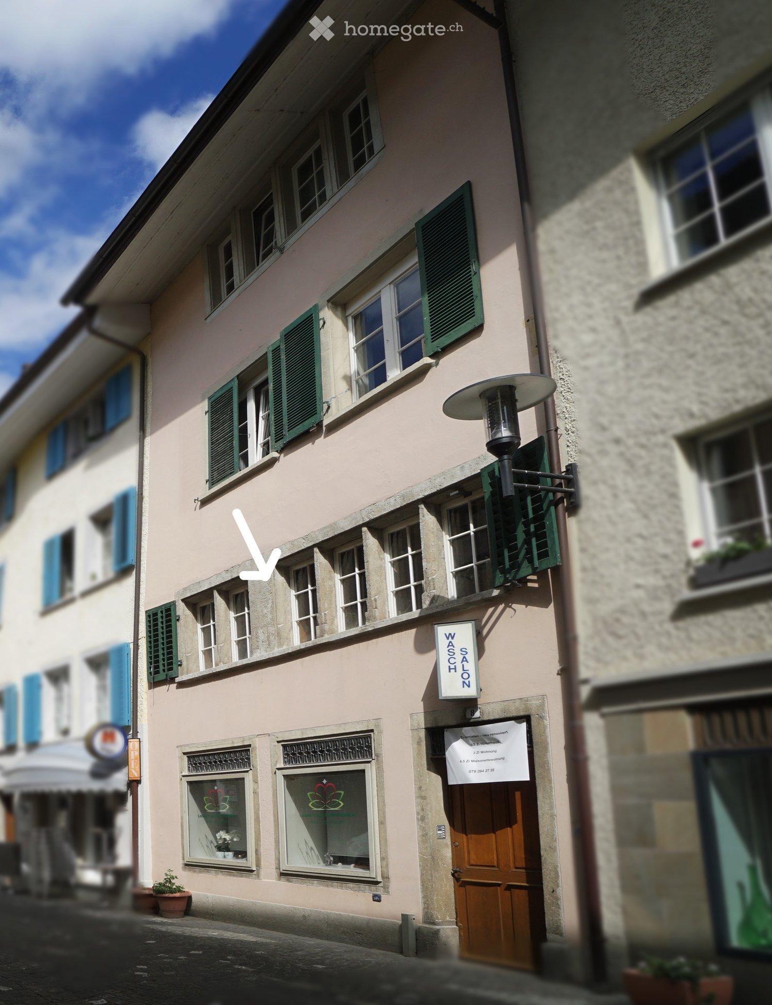 3 story building, pink exterior, green shutters, wooden door, windows with white frames, street lamp