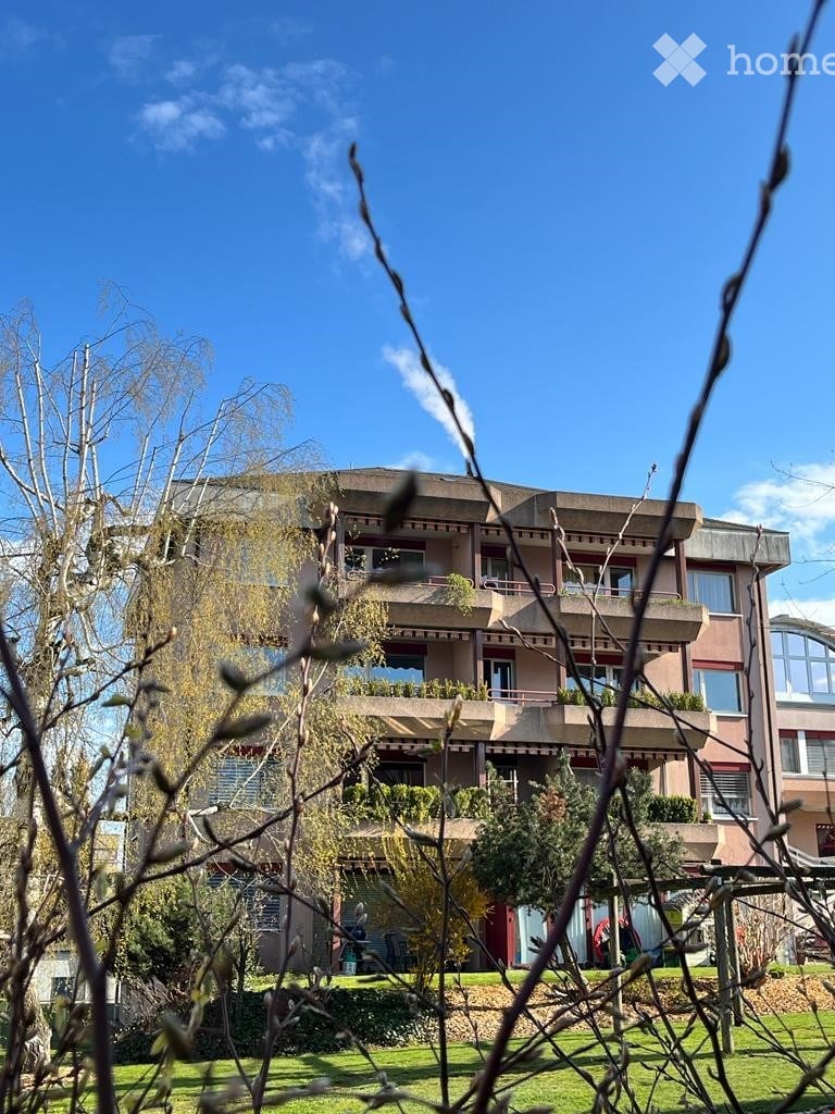 Multi-story residential building with balconies, surrounded by greenery and trees.