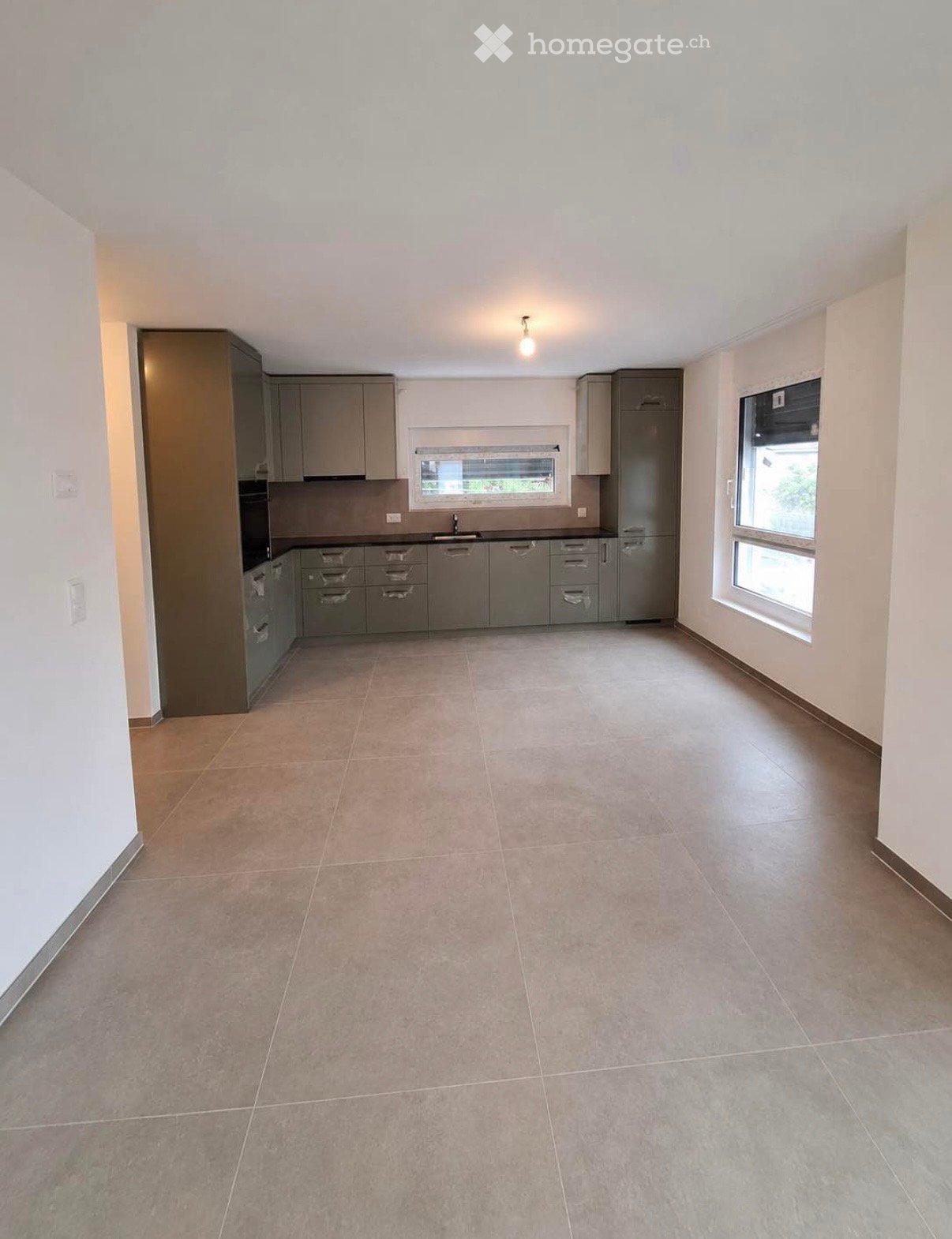 Empty kitchen with grey cabinets, tiled floor, and windows allowing natural light.