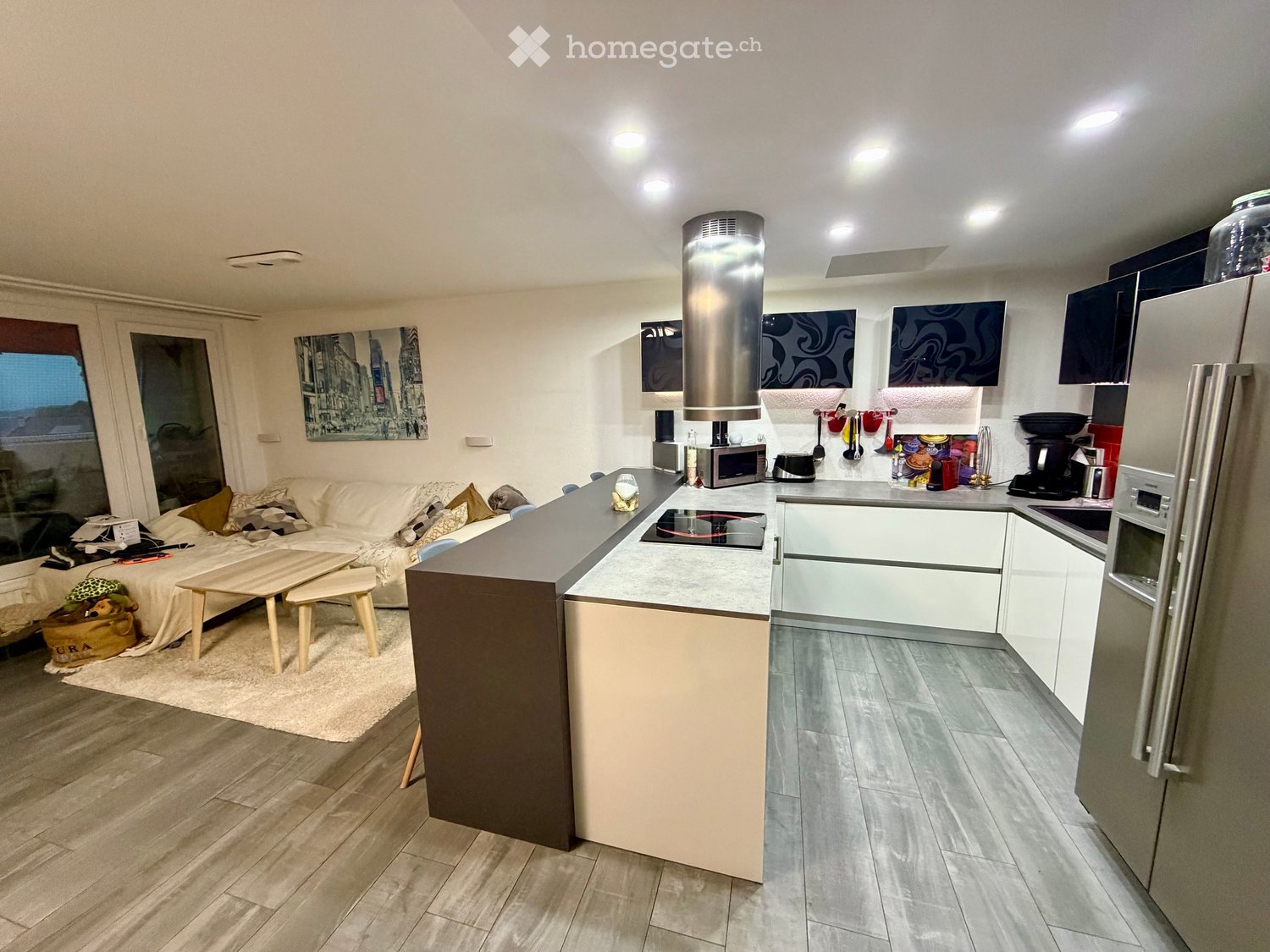 Modern open-plan living and kitchen area with a sofa, coffee table, kitchen island, and various appliances.
