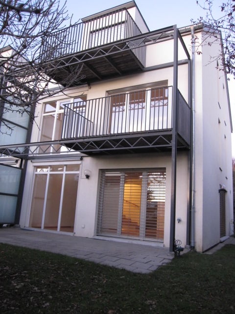 Modern two-story building with white exterior, large windows, and multiple balconies.