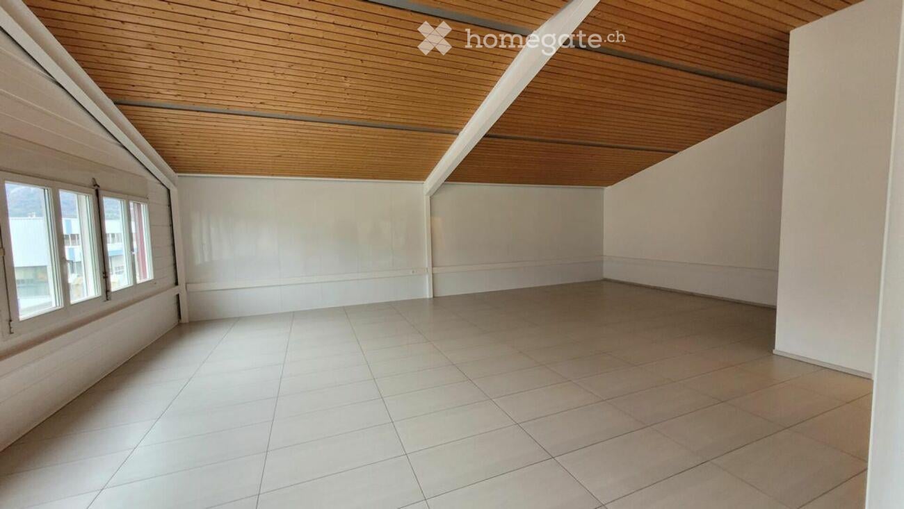Empty room with white tiled floor, white walls, and wooden slatted ceiling. Three windows on one side provide natural light.