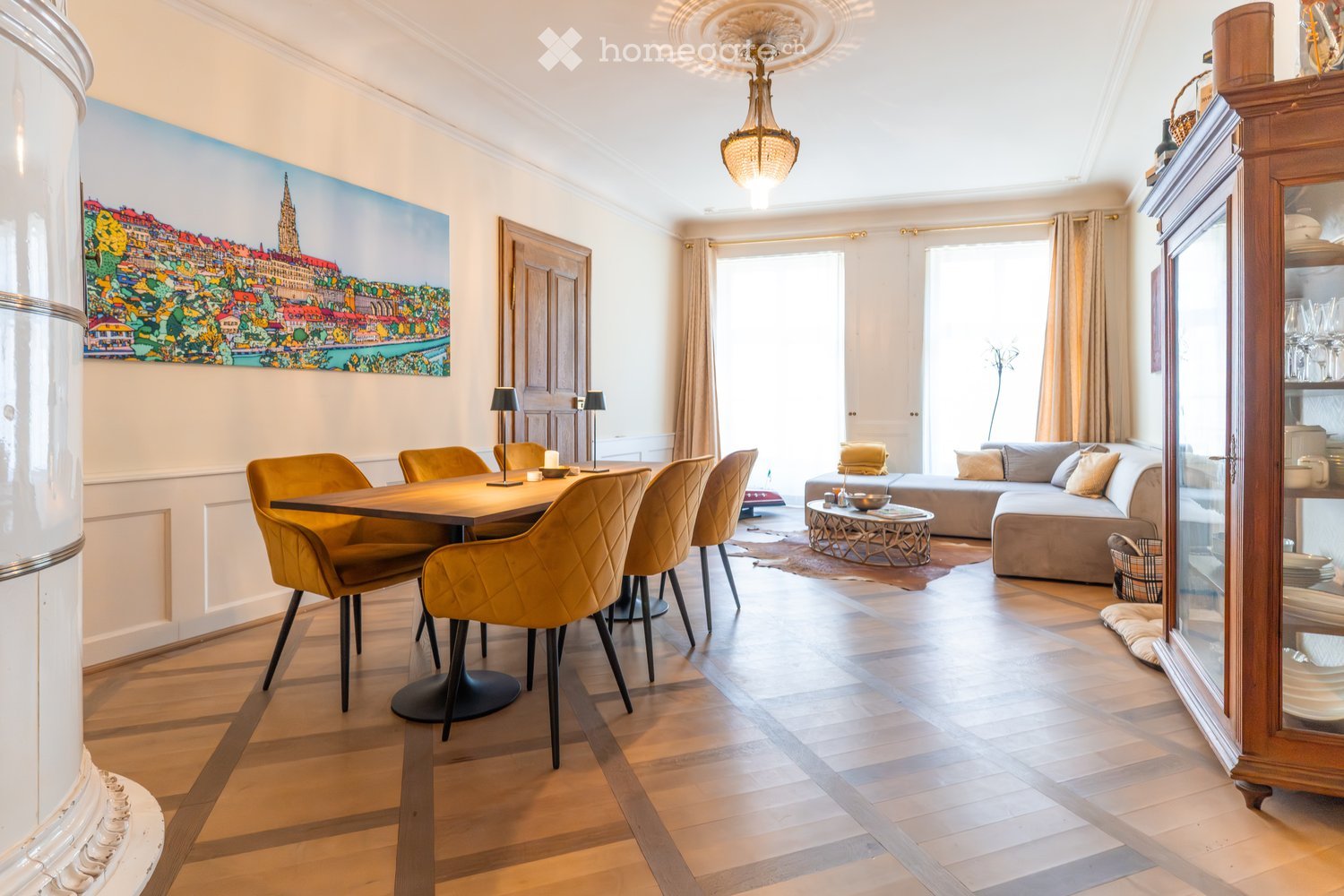 Open-plan living and dining area with wooden flooring, a large sofa, a coffee table, a dining table with chairs, and a cabinet with glass doors.