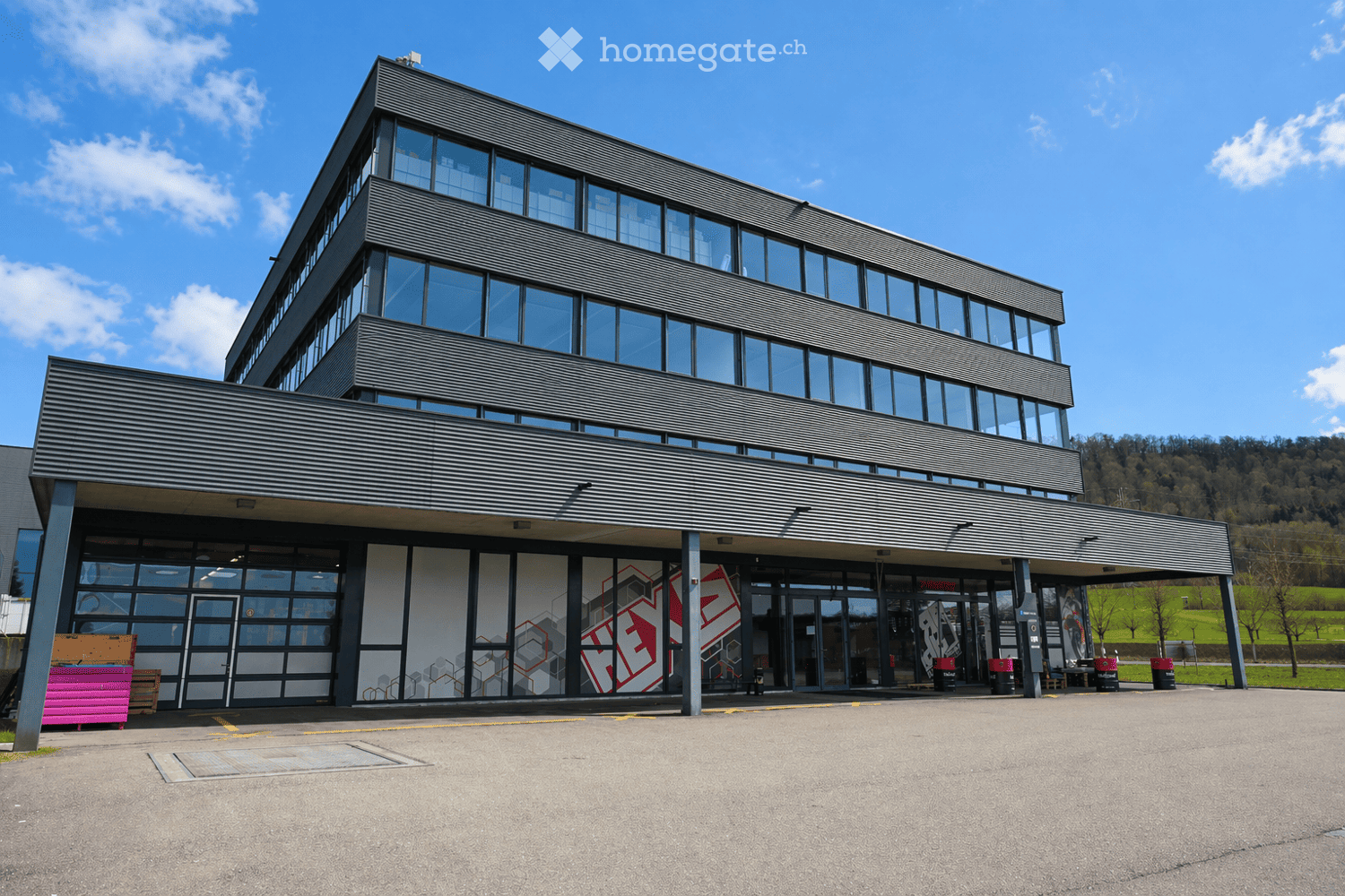 Modern two-story building with large glass windows and a sleek, angular design. The entrance features a covered walkway with geometric wall art.