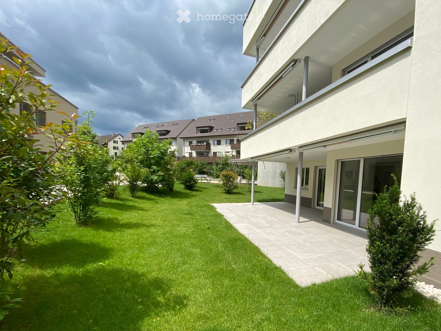 Well-maintained garden with green lawn, trimmed bushes, and a modern house with large windows and a balcony.