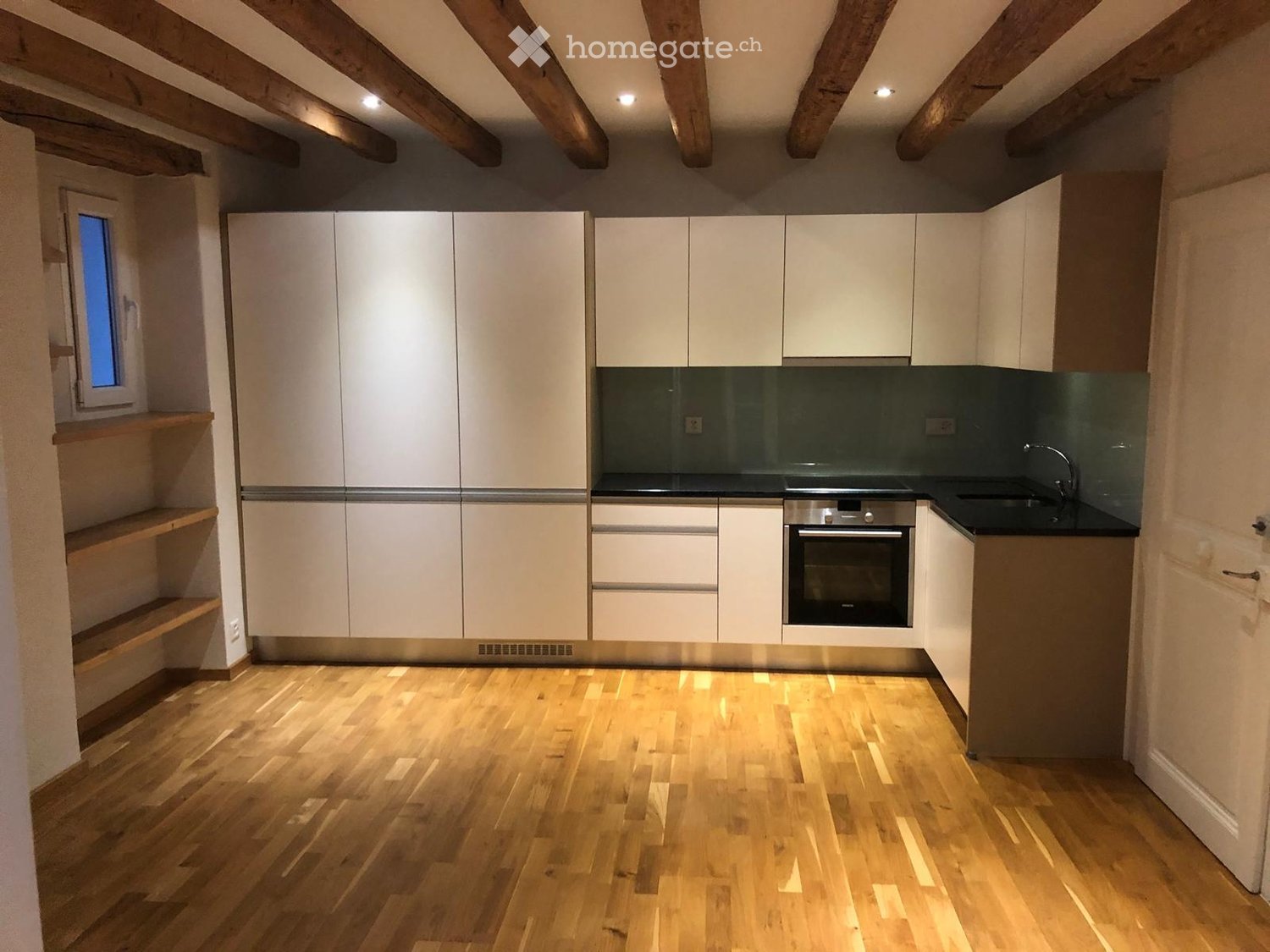 Modern kitchen with white cabinets, stainless steel oven, and wooden flooring.